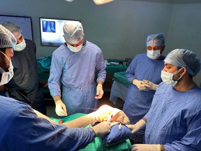 A group of surgeons, led by Dr. Ishwar Meena, a foot and ankle specialist, performing surgery in an operating room. All are wearing blue surgical gowns and masks, focusing on the procedure.