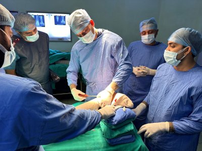 A group of surgeons, led by Dr. Ishwar Meena, a foot and ankle specialist, performing surgery in an operating room. All are wearing blue surgical gowns and masks, focusing on the procedure.