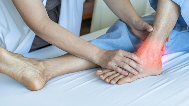 A healthcare professional examines a patient's ankle, which is highlighted in red to indicate pain or inflammation.